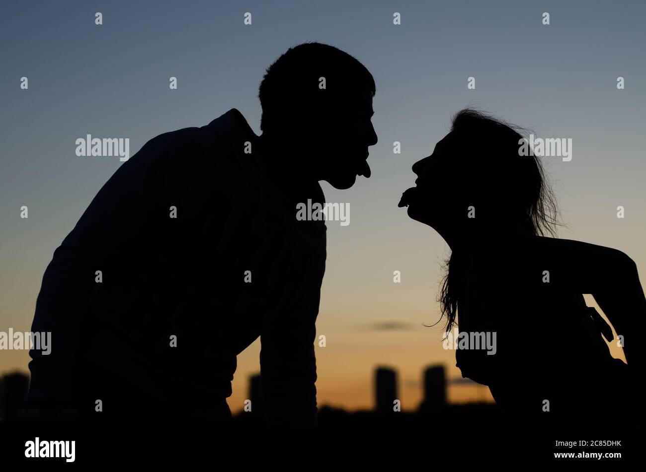 Jeune couple montrant l'autre langue contre la ville du soir Banque D'Images