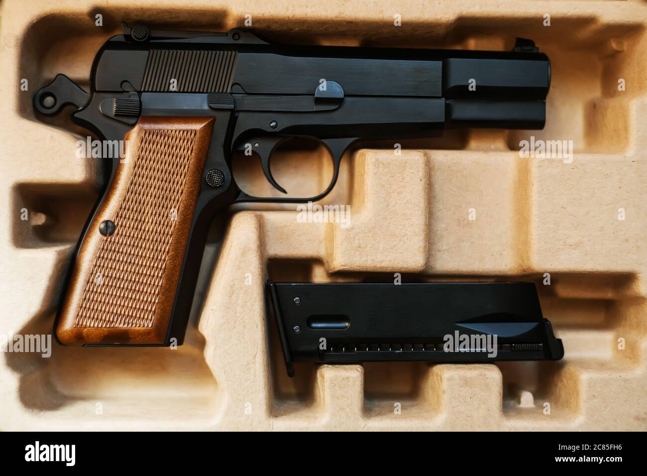Dans une boîte en carton est un pistolet airsoft avec une poignée marron, et à côté de lui est un magazine. Vente et livraison d'armes. Banque D'Images