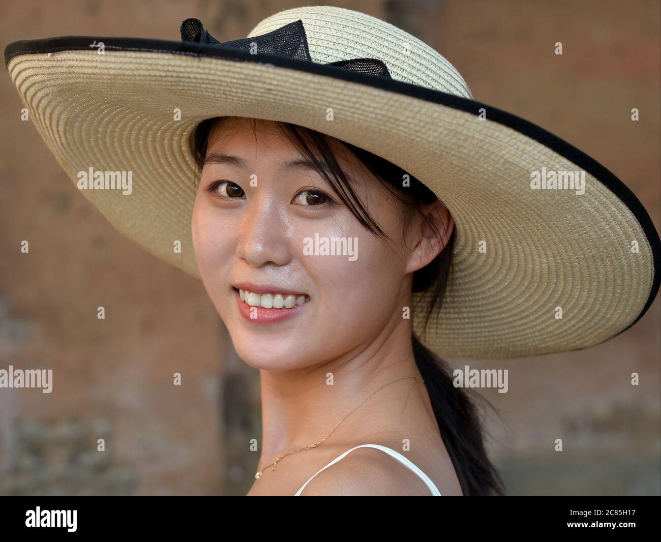 Jeune femme chinoise attrayante en vacances porte un élégant chapeau de paille à large bord et sourit pour l'appareil photo. Banque D'Images