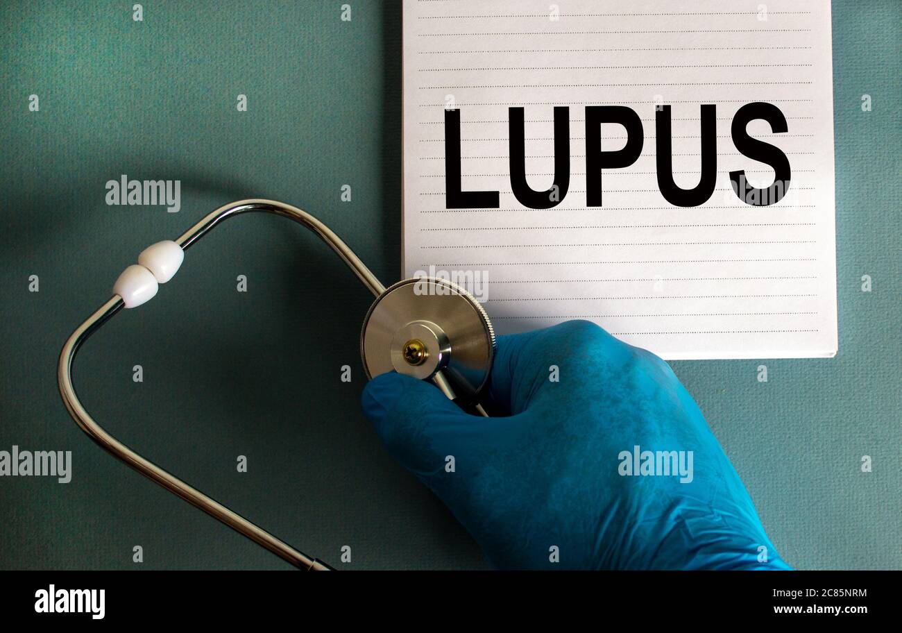 Main dans un gant bleu, carte blanche avec mot lupus et stéthoscope. Banque D'Images