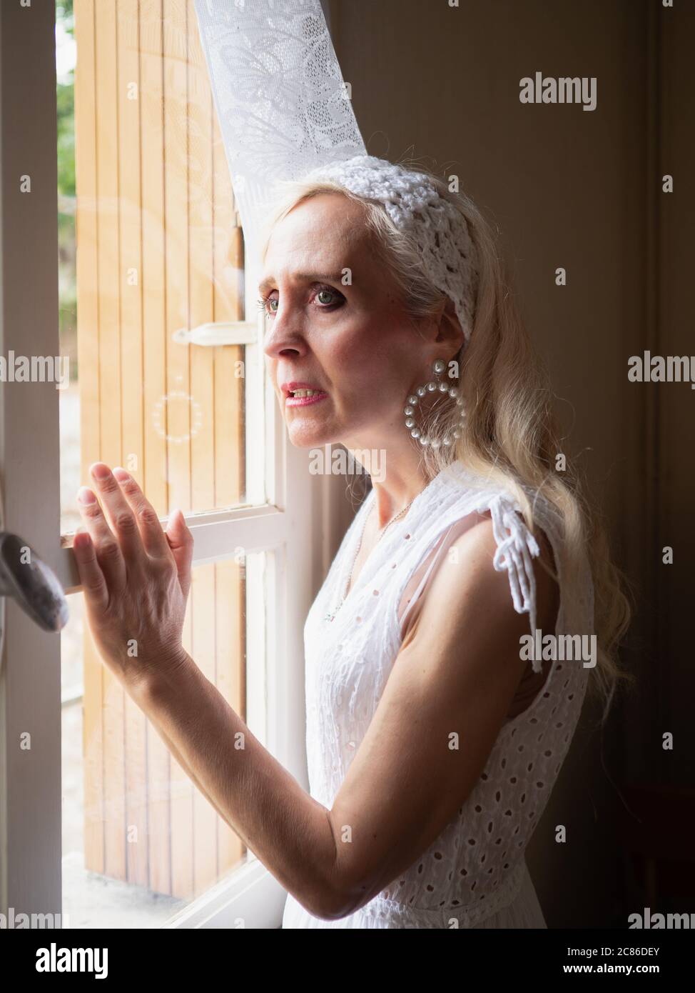 Portrait vertical d'une femme mûre et anxieuse debout et regardant à travers la fenêtre Banque D'Images