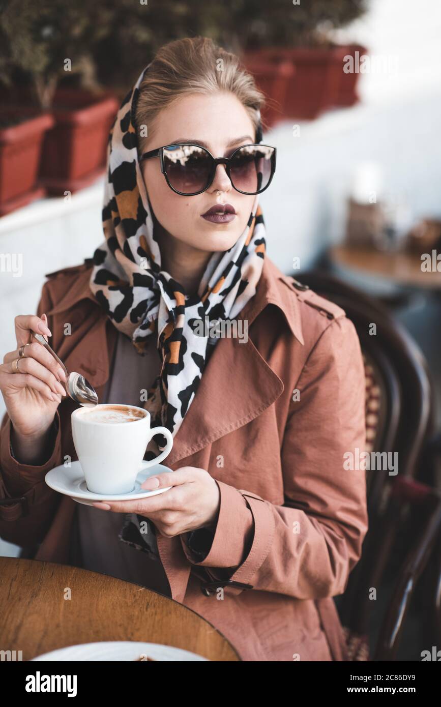 Belle femme de 24-25 ans buvant du café dans un café portant une veste  élégante, des lunettes de soleil et une écharpe en soie à l'extérieur Photo  Stock - Alamy