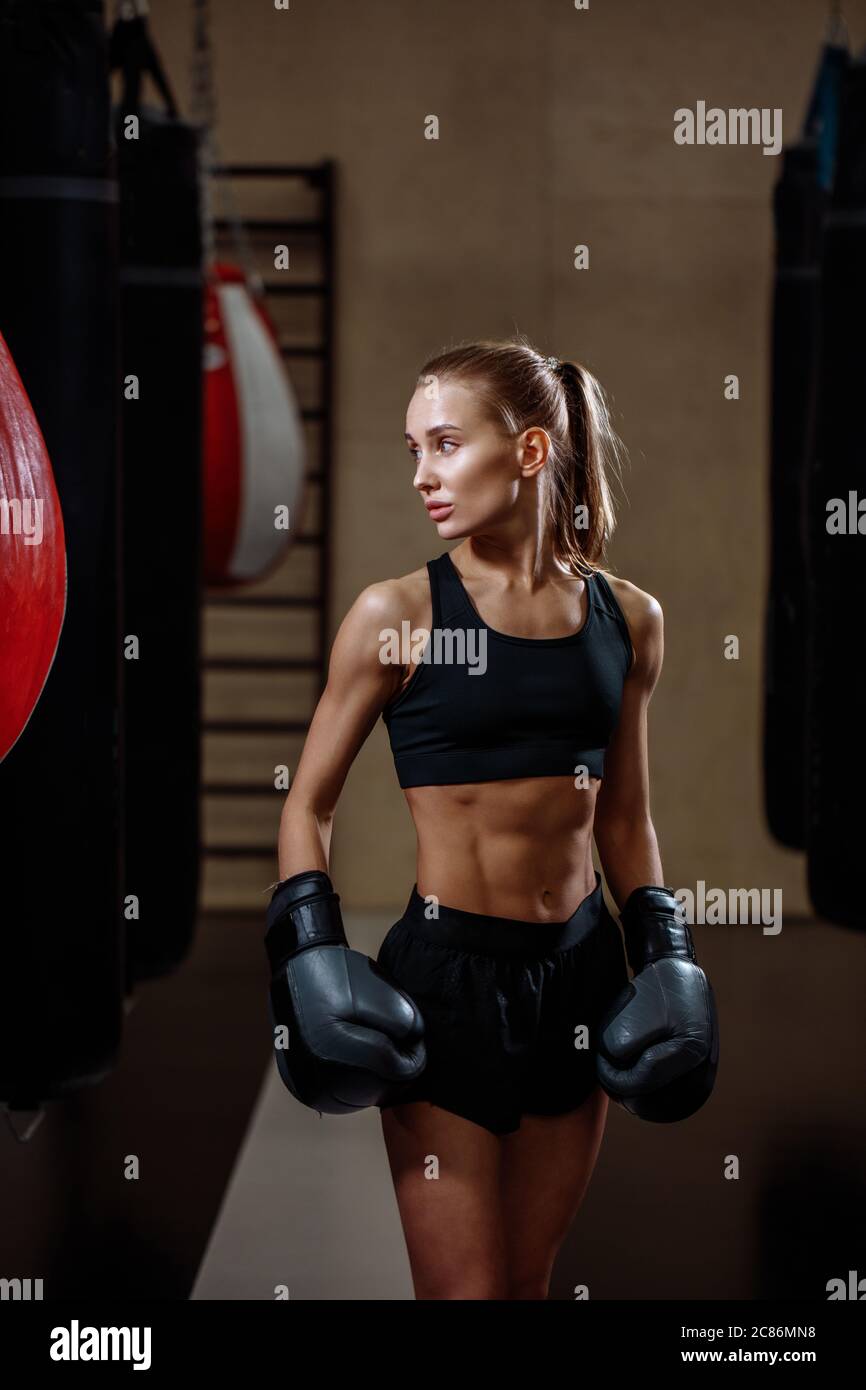 blonde fille en gants de boxe noirs posant dans la salle de gym Banque D'Images