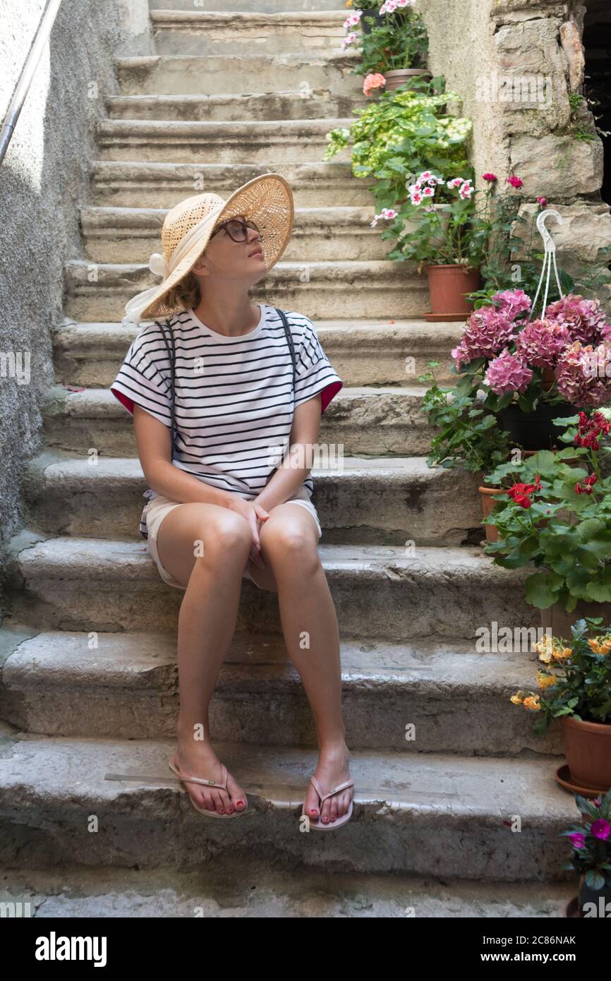 Belle touriste femme portant un grand chapeau de paille et un short assis  et reposant sur les escaliers de la maison en pierre ancienne pendant les  voyages d'été sur la Méditerranée Photo