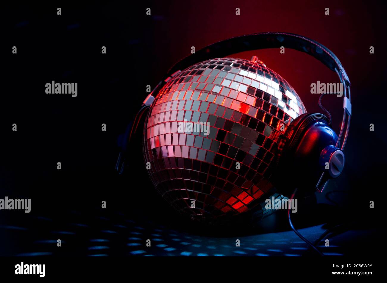 Concept de musique et de vie nocturne de discothèque avec une pochette de bal disco dans un miroir, avec écouteurs reflétant la lumière rouge et bleue dans un club sombre avec copie Banque D'Images