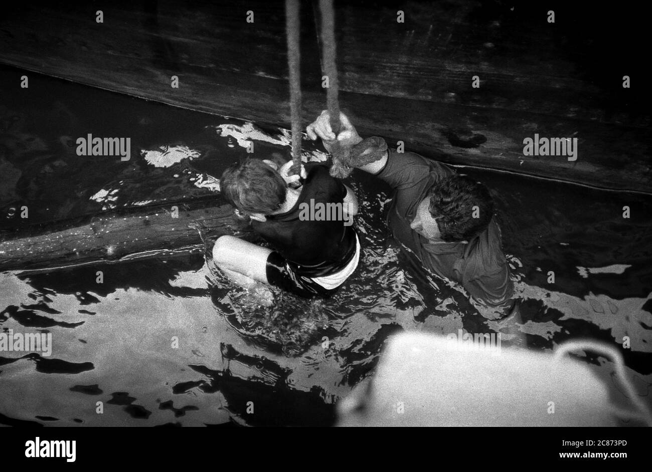 AJAXNETPHOTO. 8 JUIN 1969. PORTSMOUTH, ANGLETERRE. - LE HÉROS SAUVE L'ENFANT - ROGER BAYLISS (8YRS) A GLISSÉ ET EST TOMBÉ DU MUR NORD DU QUAI DE CARROSSAGE DANS LES EAUX MURKEY À 15 PIEDS EN DESSOUS. COINCÉ ENTRE LE MUR DU QUAI ET UNE BARGE BRITANNIQUE DES SERVICES ROUTIERS ET EN DANGER D'ÊTRE ÉCRASÉ, IL A ÉTÉ SECOURU PAR MR WARD, UN PASSAGER DANS UN VÉHICULE DE VOYAGE QUI A FAIT DES PASSES INESSÉES DANS LE QUAI, NAGÉ SOUS LA BARGE ET EST VENU EN AIDE À ROGER, UN NON NAGEUR, TANDIS QUE LES ASSISTANTS DOCKSIDE ONT TRANSPORTÉ LA PAIRE EN SÉCURITÉ. PHOTO:JONATHAN EASTLAND/AJAX REF:356923 202206 57 Banque D'Images