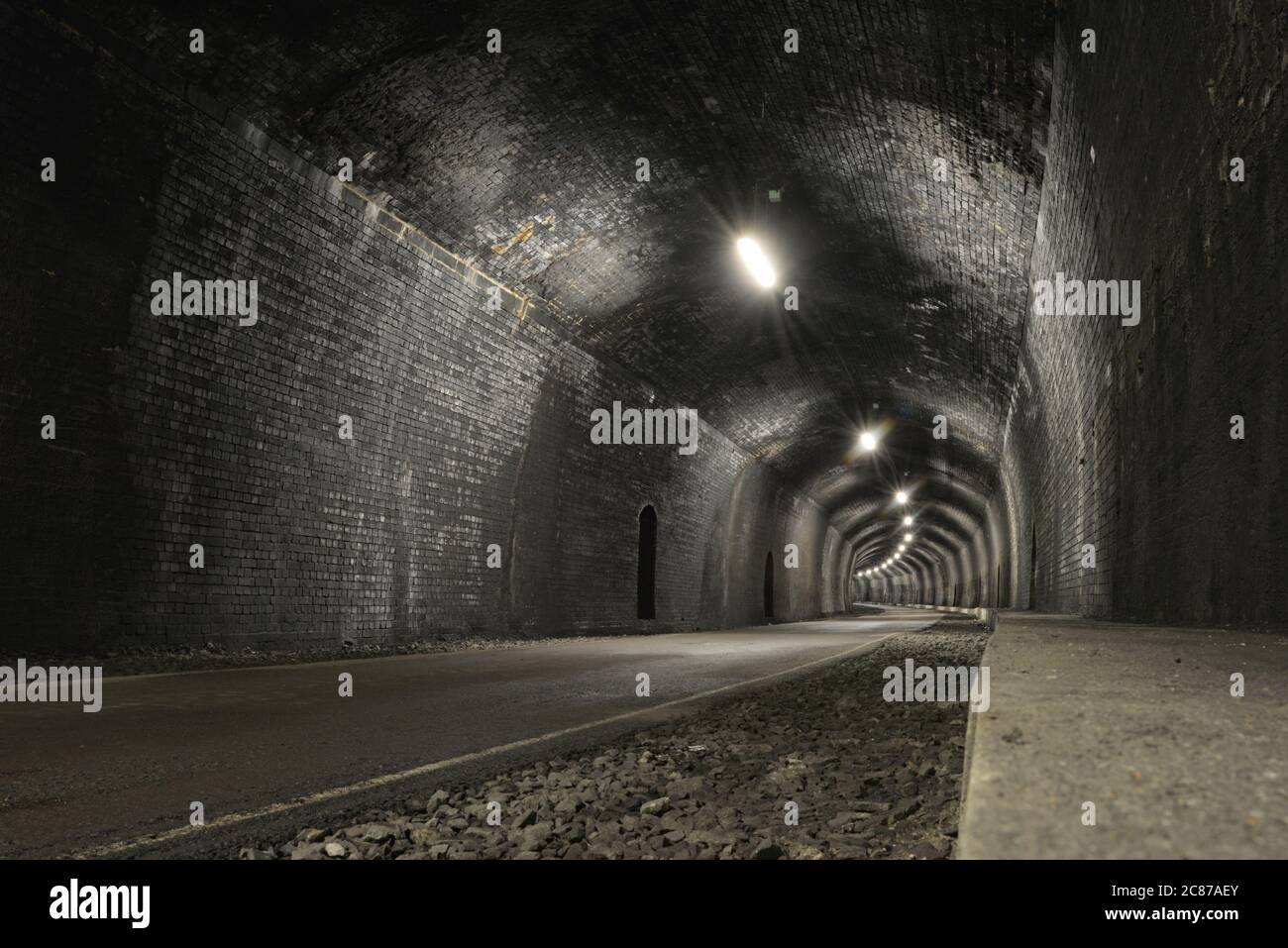 La route de la piste Monsal passe par le tunnel de la pierre d'angle, fait de briques gris foncé, une image basse et grand angle, espace vide et de copie. Tunnel ancien et rustique. Banque D'Images