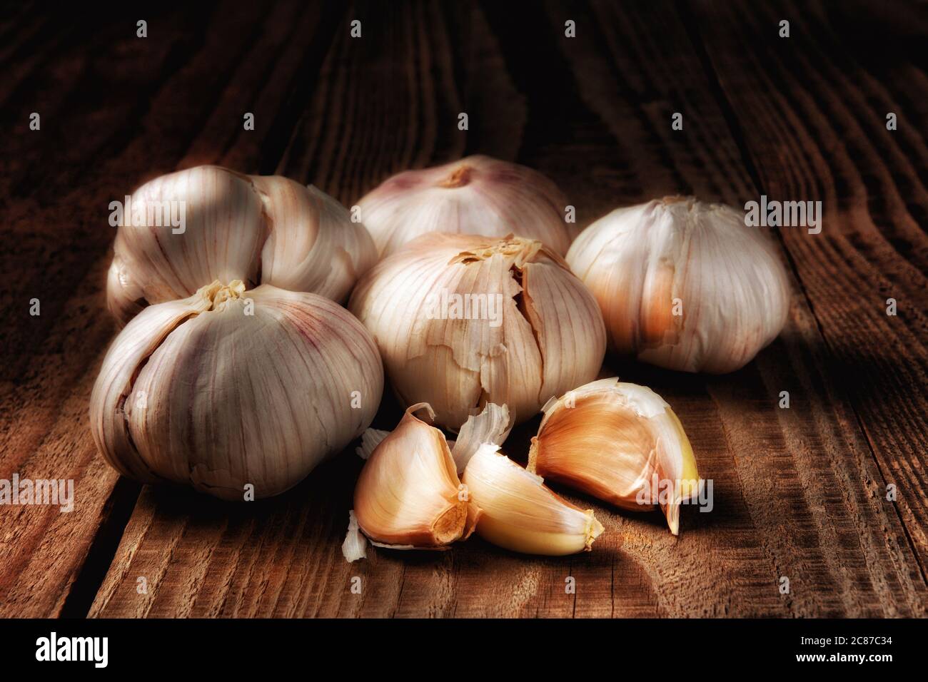 Gros plan d'un groupe de gousses d'ail italiennes sur une table en bois rustique foncé. Peinture légère vie morte. Banque D'Images