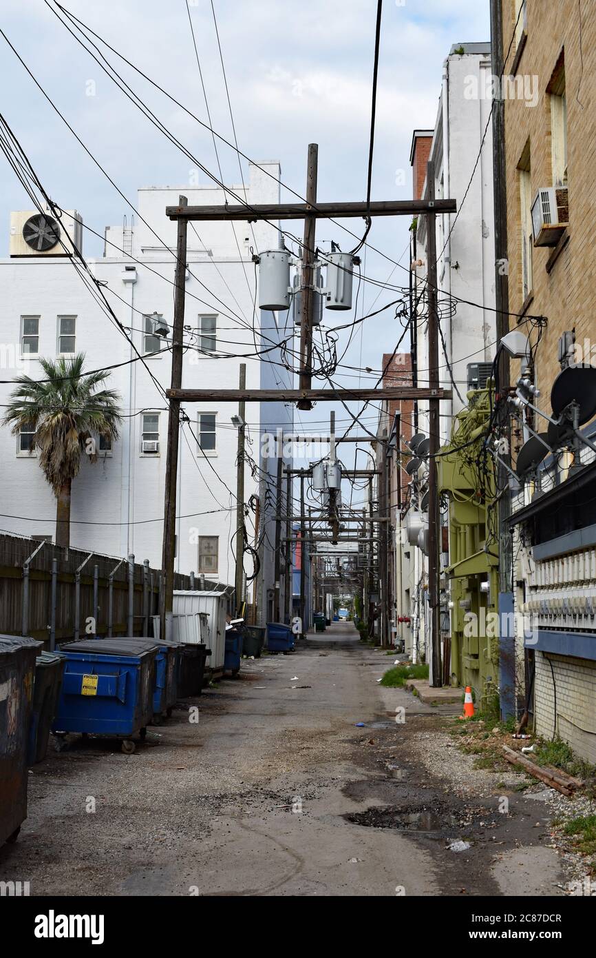 Une ruelle urbaine à Galveston, Texas. Les fils électriques ci-dessus disparaissent dans la longue rue latérale qui a des bennes le long du côté et des bâtiments. Banque D'Images