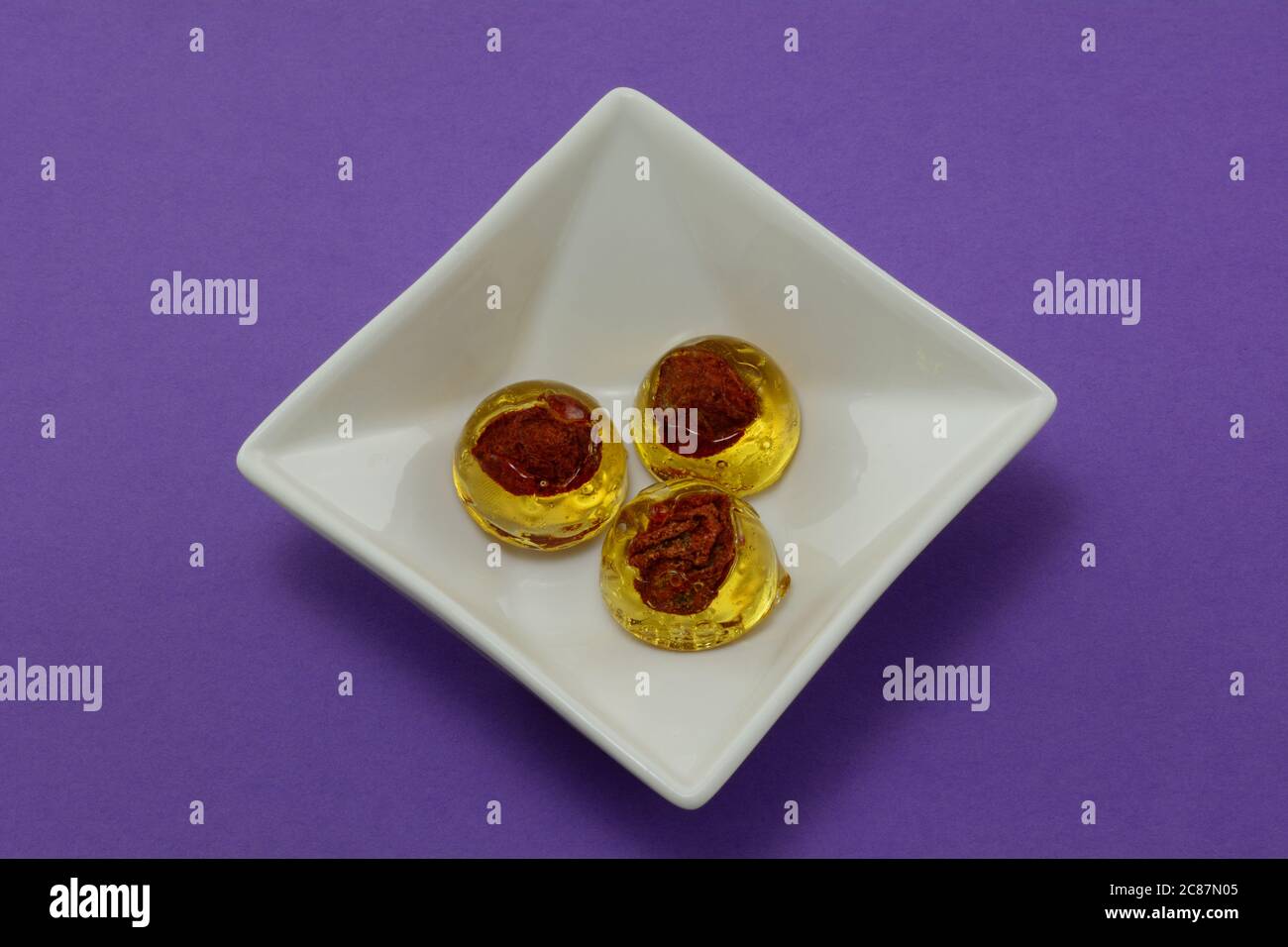 Bonbons durs aux prunes avec une fosse au centre dans un plat de bonbons blanc sur fond violet Banque D'Images