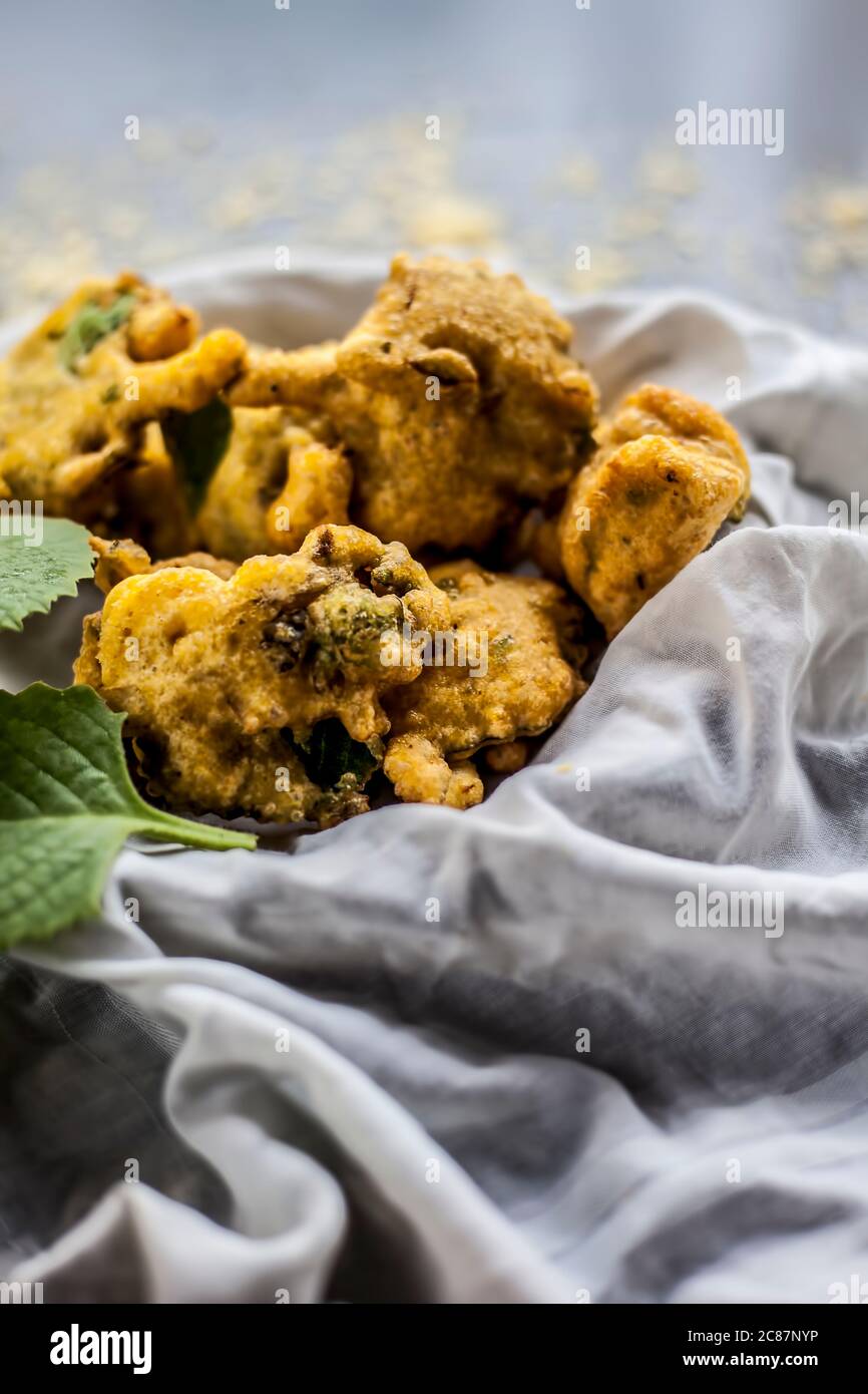 Gros plan de la collation de mousson ajwain pakora dans un récipient avec une feuille fraîche d'ajwain avec elle sur une surface avec un peu de farine de pois chiches saupoudrées Banque D'Images