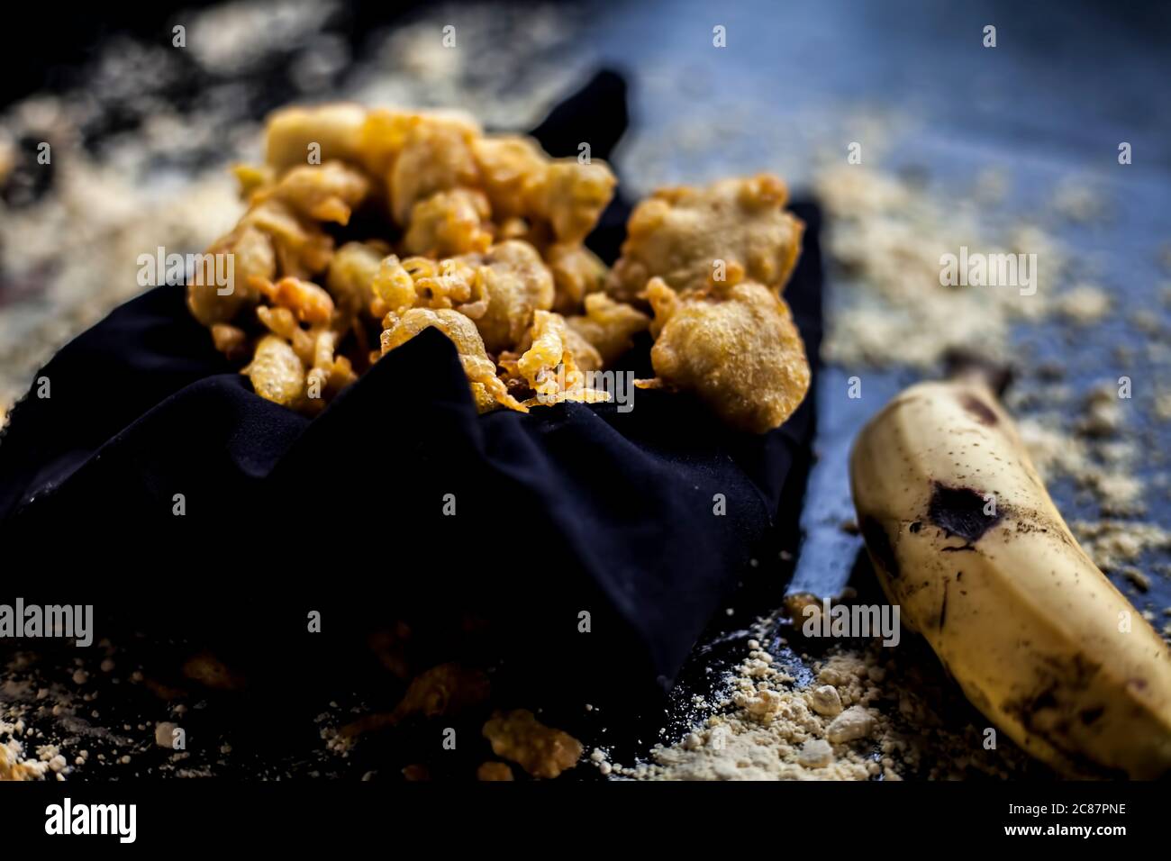 Le fameux coup de banane bhajia dans un contenant de couleur noire avec quelques bananes crues et des épices qui sont nécessaires pour le faire. Banque D'Images