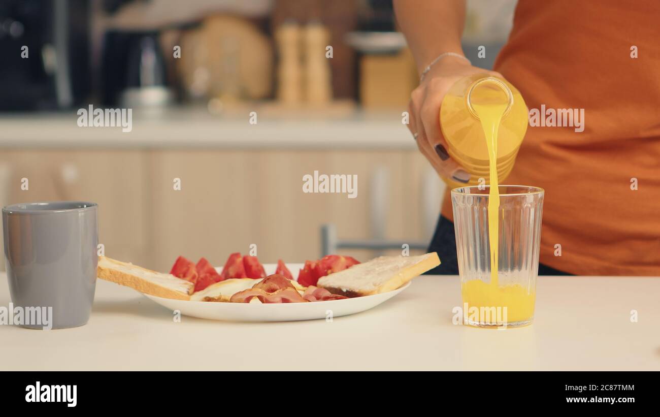Femme versant du jus frais dans le verre pour le petit déjeuner dans la cuisine. Femme qui boit du jus d'orange sain et naturel. Femme au foyer boire du jus d'orange maison sain et naturel. Rafraîchissement le dimanche matin Banque D'Images