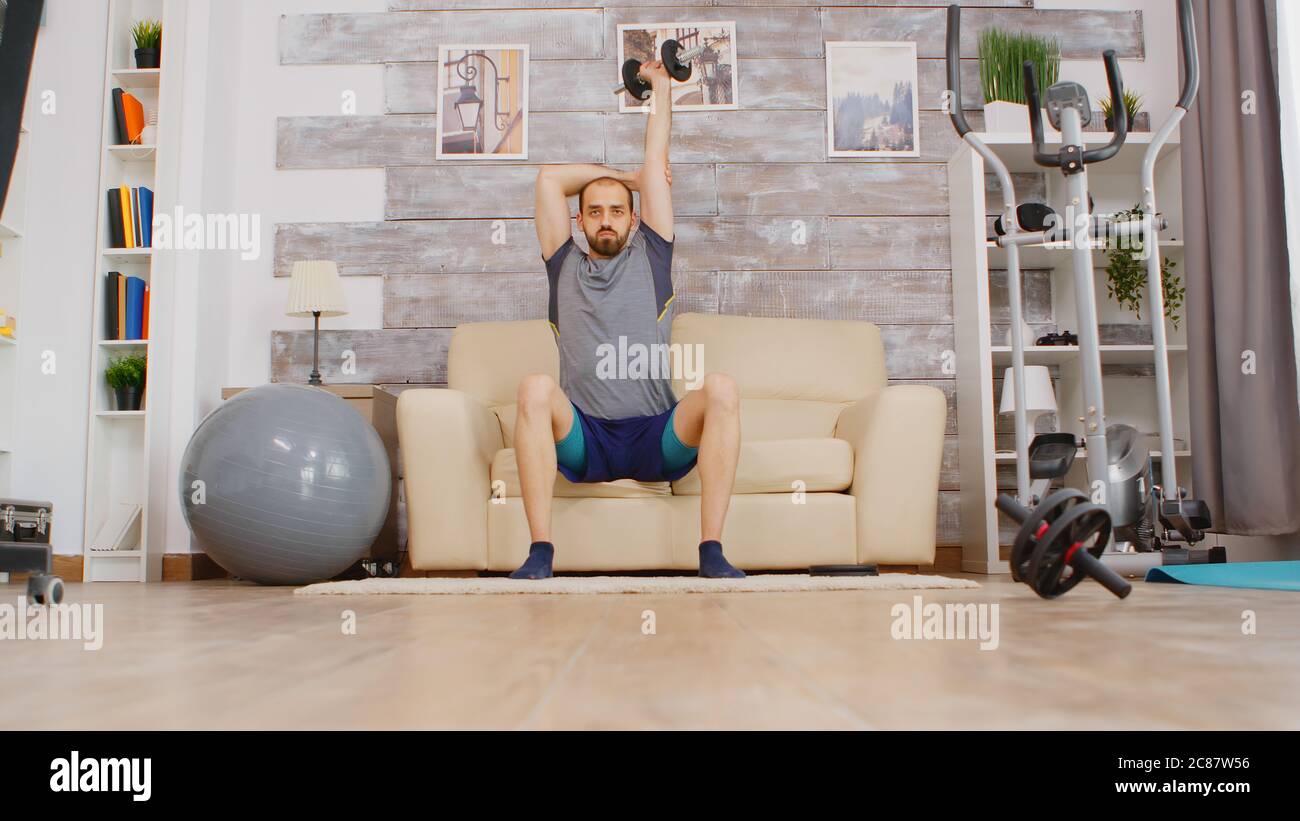 Guy lever haltères avec triceps muscle portant vêtements de sport assis o canapé. Banque D'Images