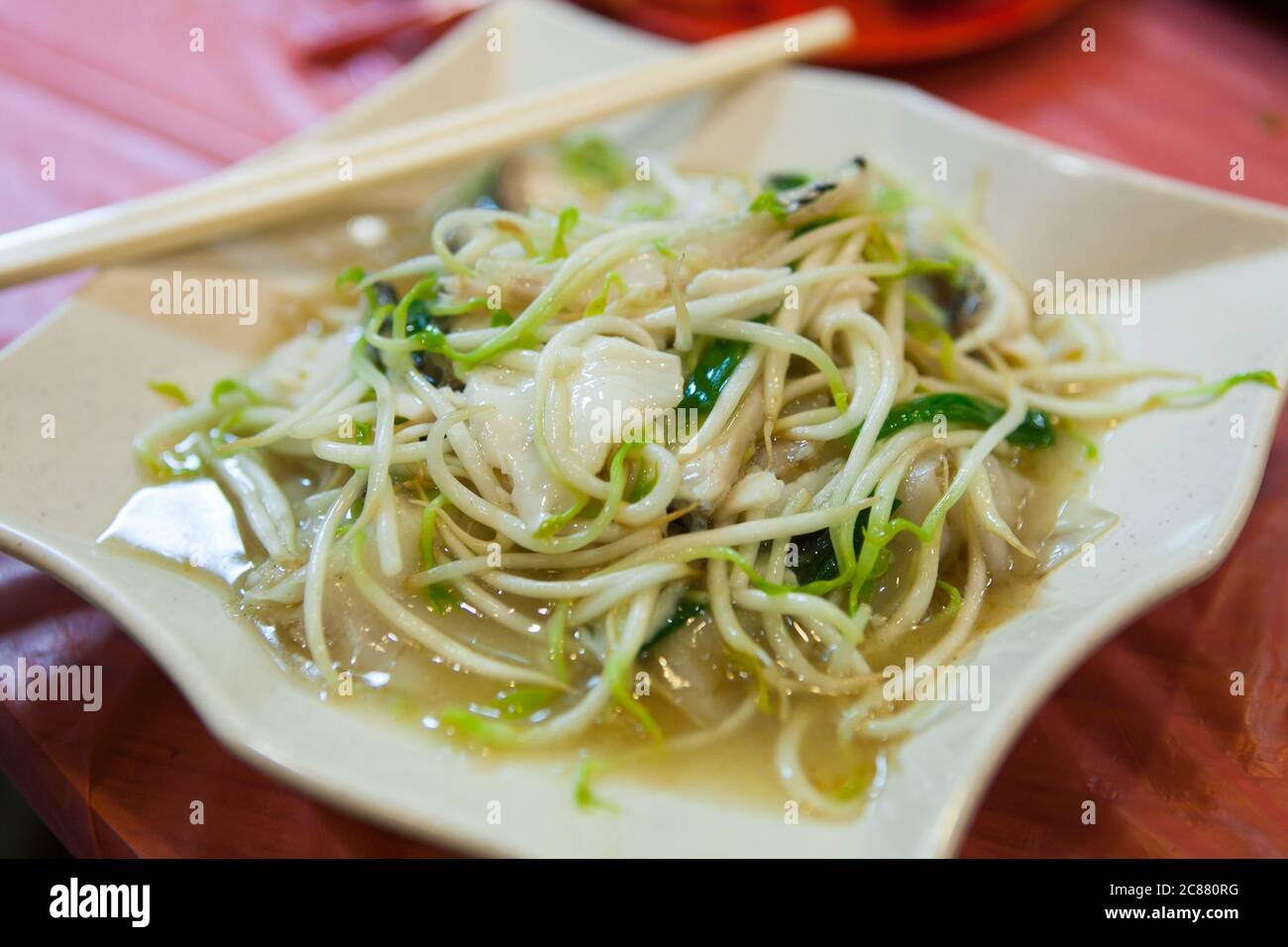 Remuer le germe de haricot frit et quelques morceaux de chair de poisson sur l'assiette de service blanche. Servi parmi tout le monde sur la table. Banque D'Images
