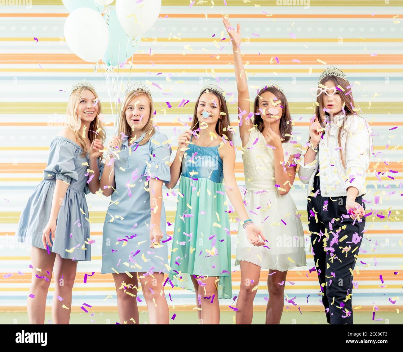 Jolies filles adolescentes souriantes en robes joyeuses mains levées ensemble et courir des sous-vêtements avec des sparkles et des balons à la fête d'anniversaire o Banque D'Images