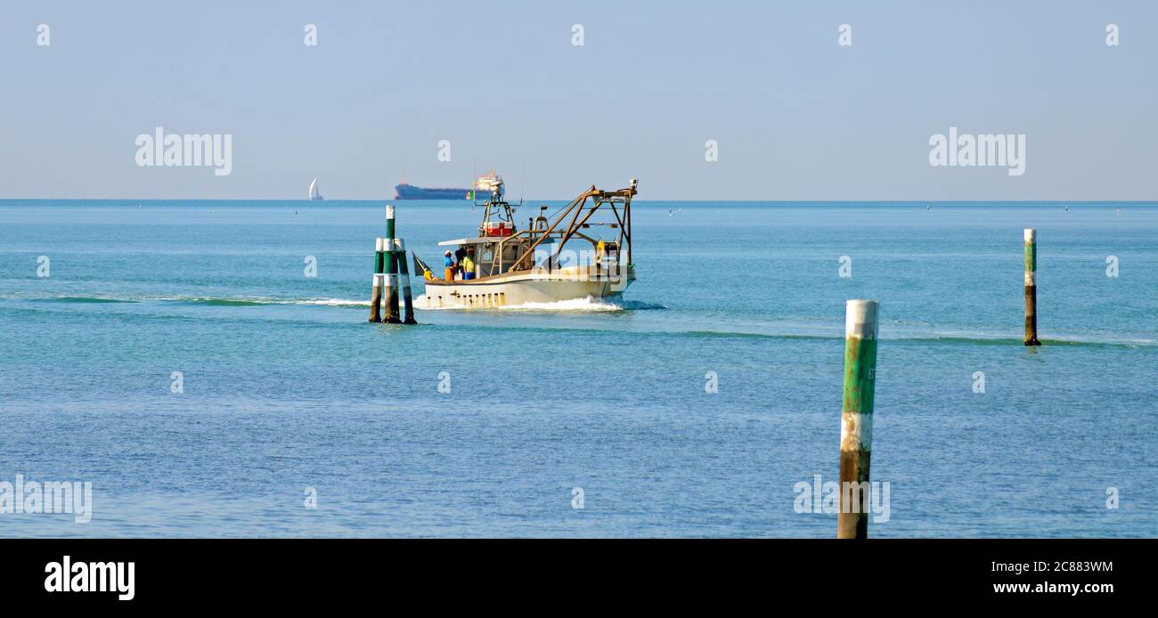 Bateau de pêche sur un voyage à domicile entre les marques de voies navigables sur la mer Adriatique supérieure près de Grado avec un bateau-citerne à l'horizon, Italie Banque D'Images