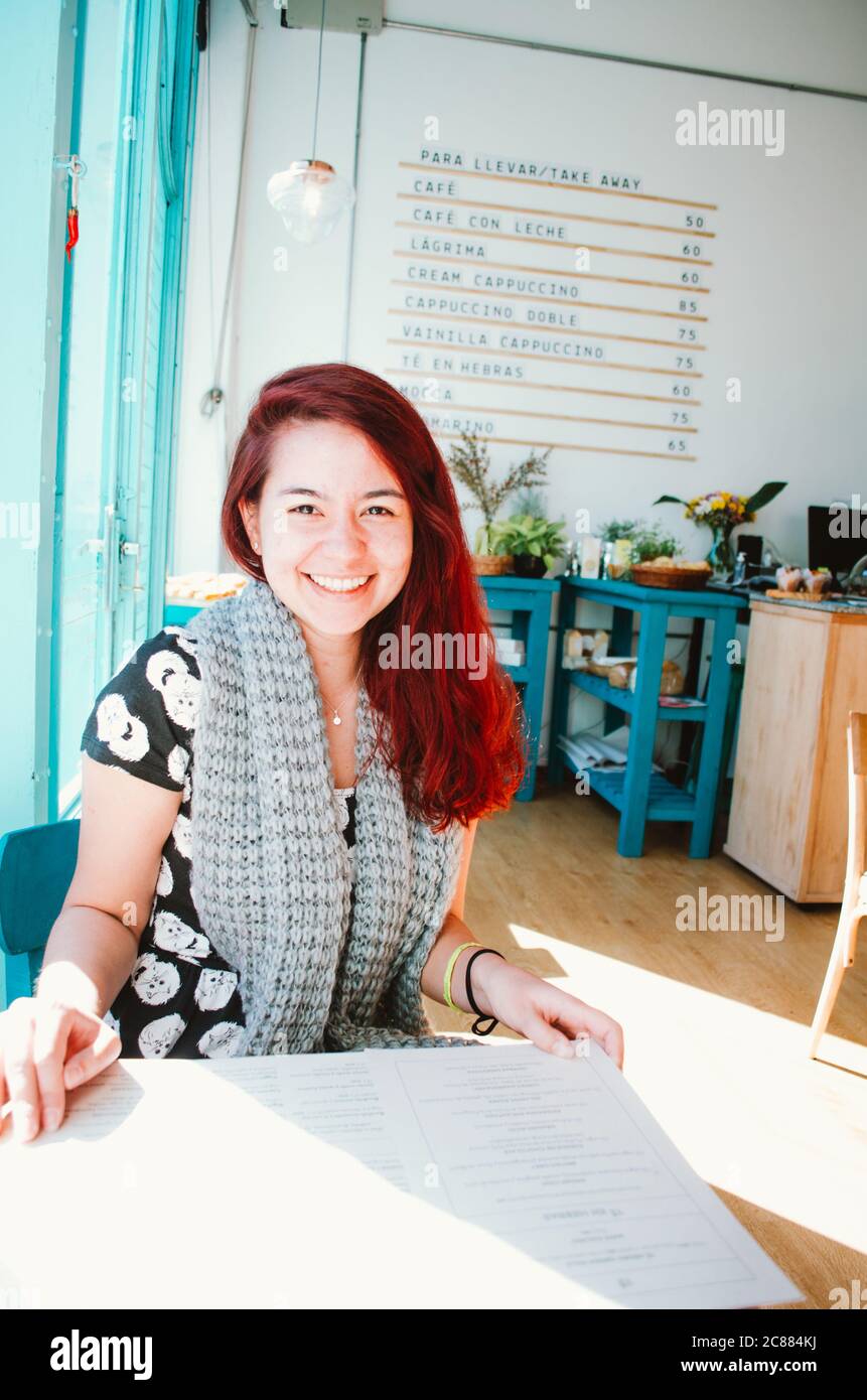 Une femme brésilienne à tête rouge dans ses 20 ans souriant tout en s'asseyant dans un café à thème turquoise qui a récemment ouvert dans le quartier de San Telmo. Banque D'Images