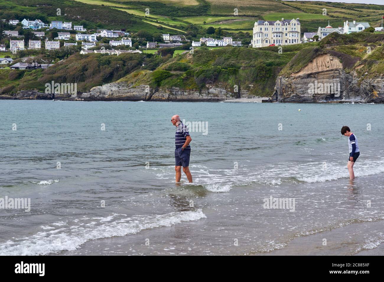 Homme plus âgé en short et jeune garçon pagayant tous les deux dans la mer à Port Erin, île de Man Banque D'Images