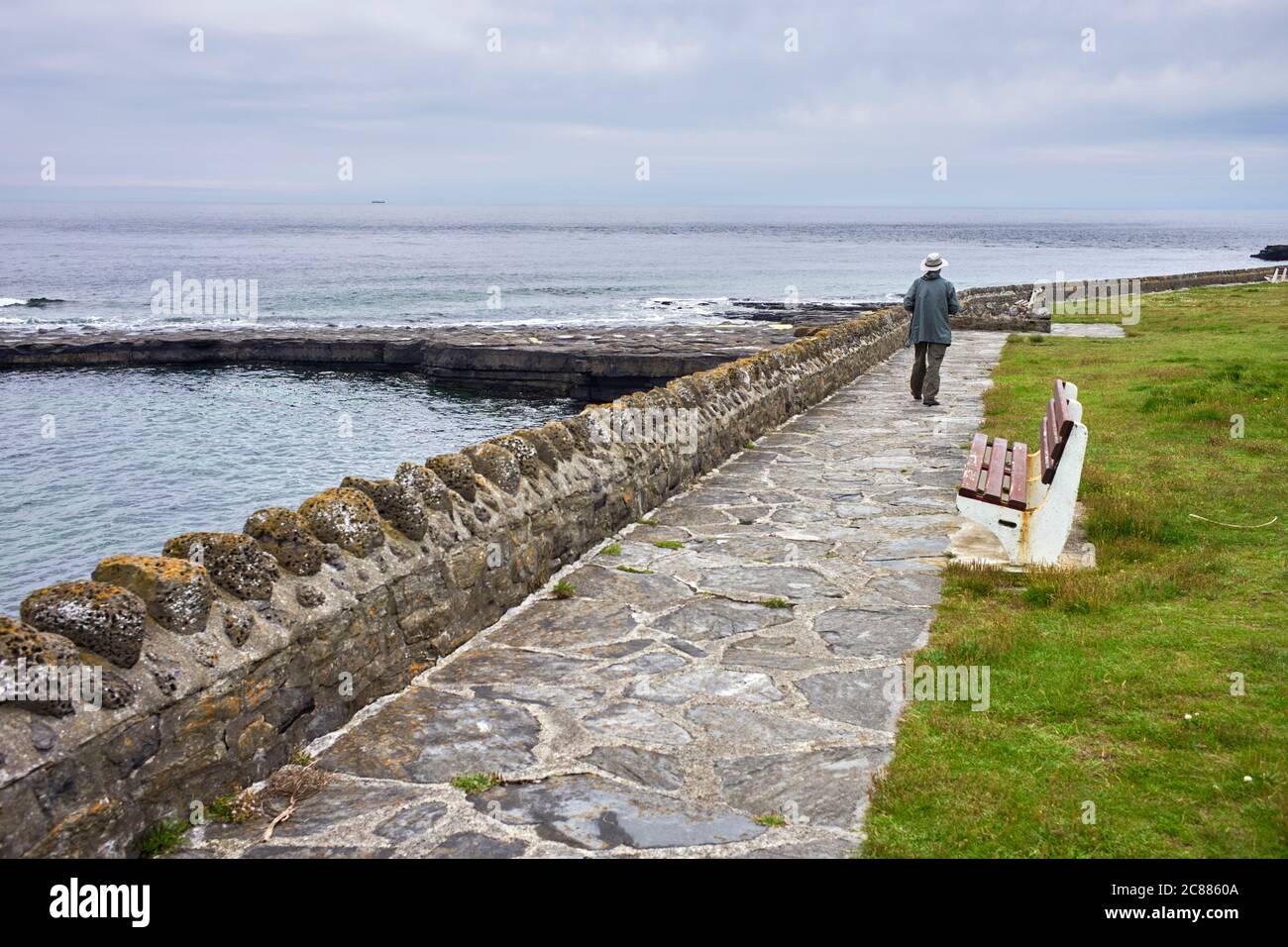 Homme plus âgé portant un chapeau vu de derrière, marchant au bord de la mer à Port St Mary, île de Man Banque D'Images