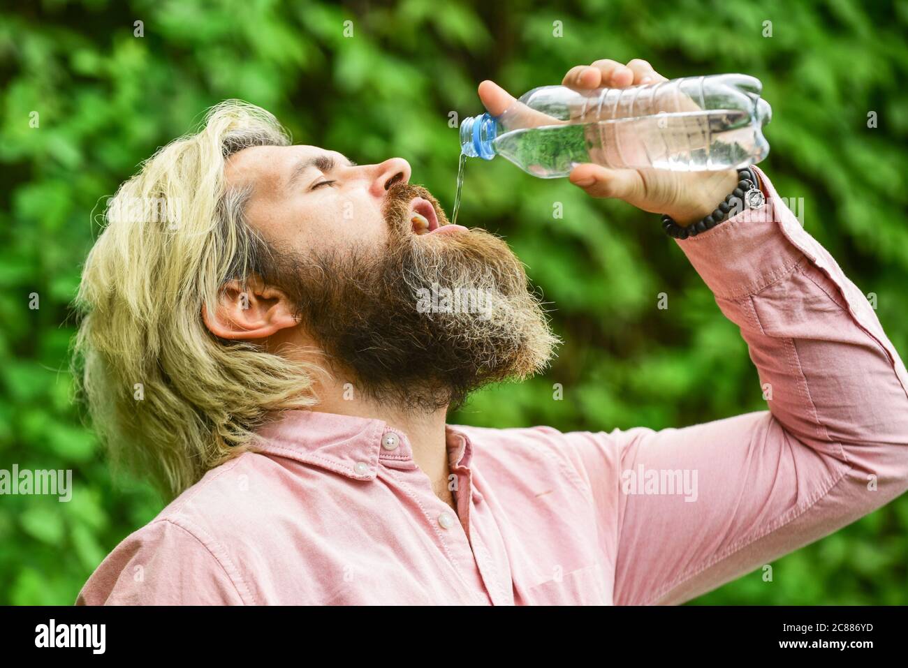 Équilibre de l'eau. Homme barbu touriste eau potable bouteille plastique nature fond. Chaleur estivale. Boire de l'eau claire. Un gars assoiffé qui boit de l'eau en bouteille Un mode de vie sain. Sécurité et santé. Banque D'Images