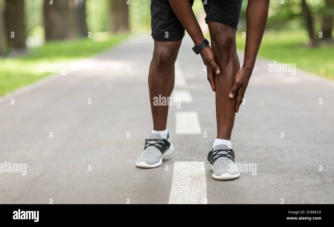 Un sportif noir touche sa jambe de sport tout en faisant du jogging à l'extérieur Banque D'Images