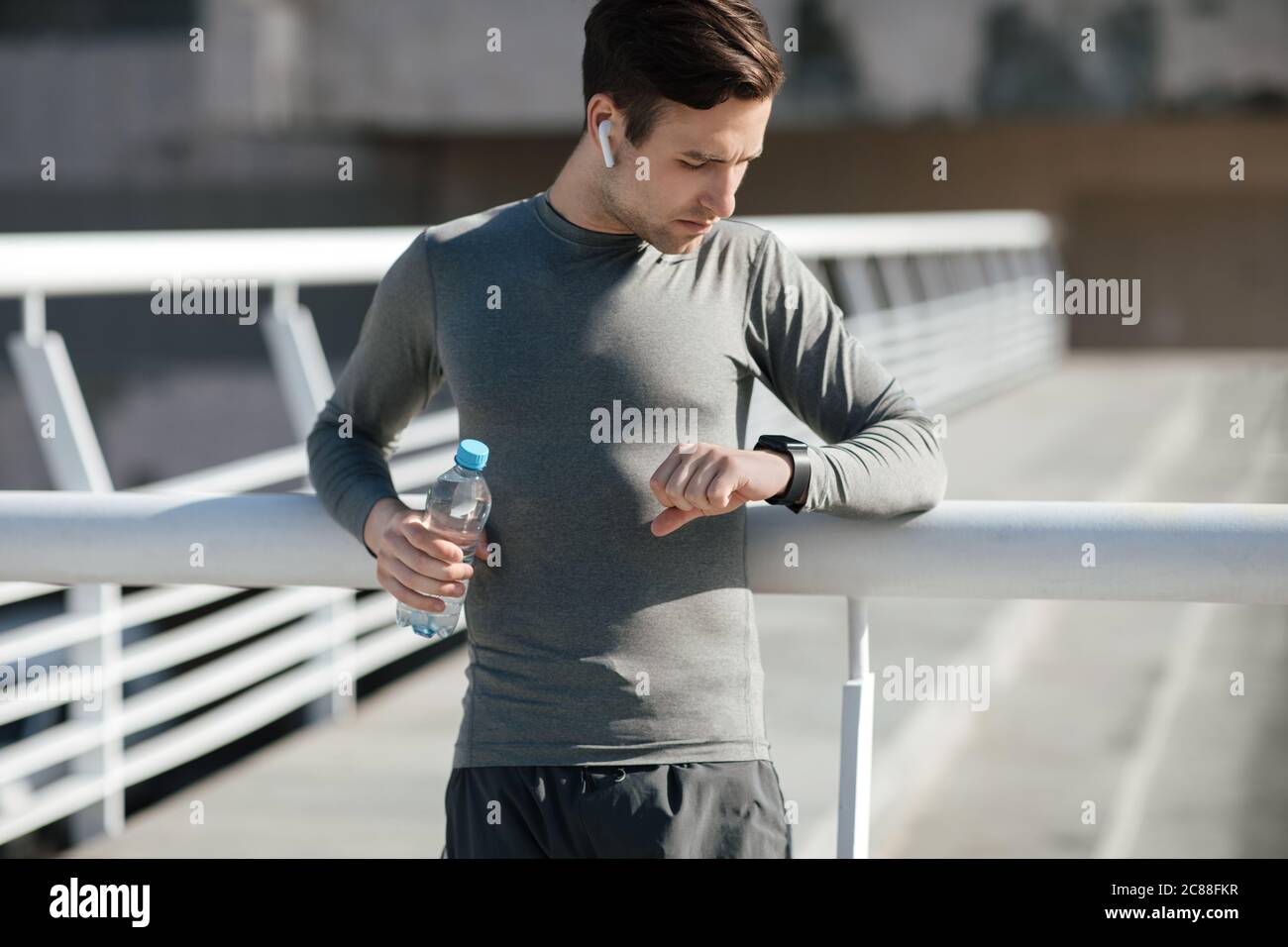 Un gars musclé avec un casque et une bouteille d'eau regarde la montre de fitness Banque D'Images