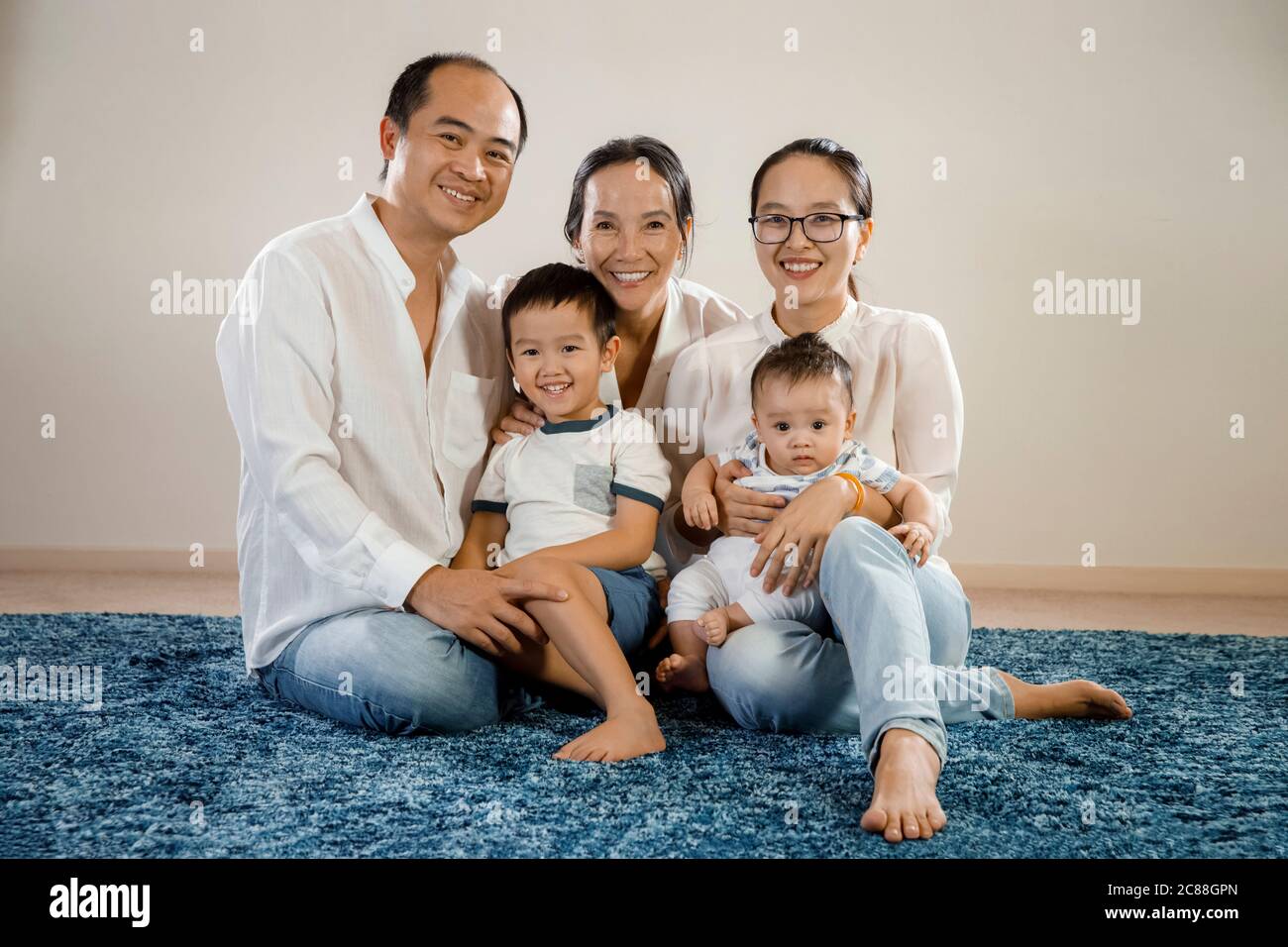 une famille asiatique heureuse assise ensemble portrait, tapis bleu sur fond blanc sur le sol, concept de famille asiatique est multi-génération, souriant embrassant Banque D'Images