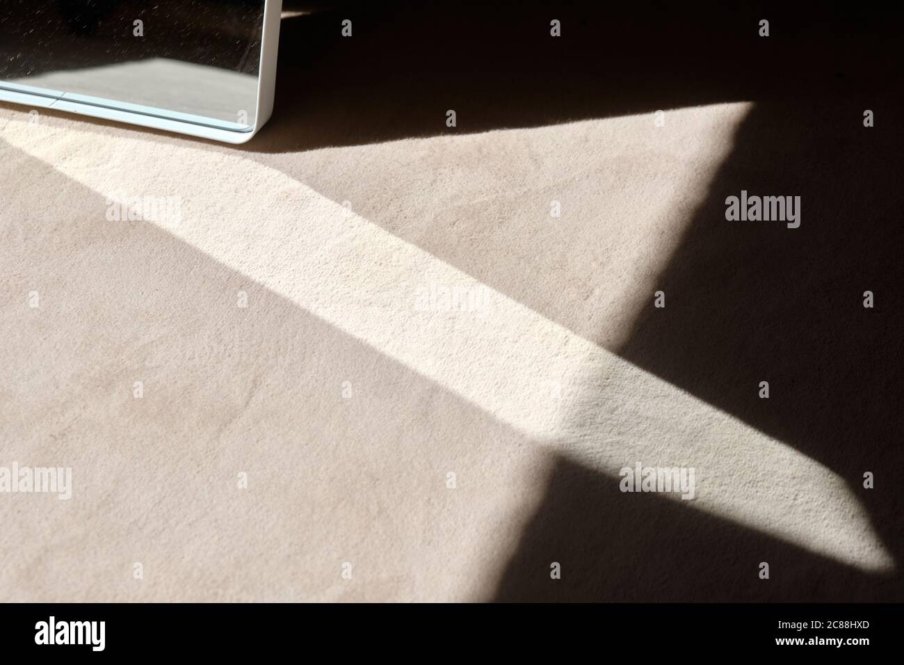 Arrière-plan abstrait tourné avec la lumière du soleil qui brille à travers une fenêtre et réfléchi par un miroir sur un tapis beige sur le sol avec ombre noire Banque D'Images