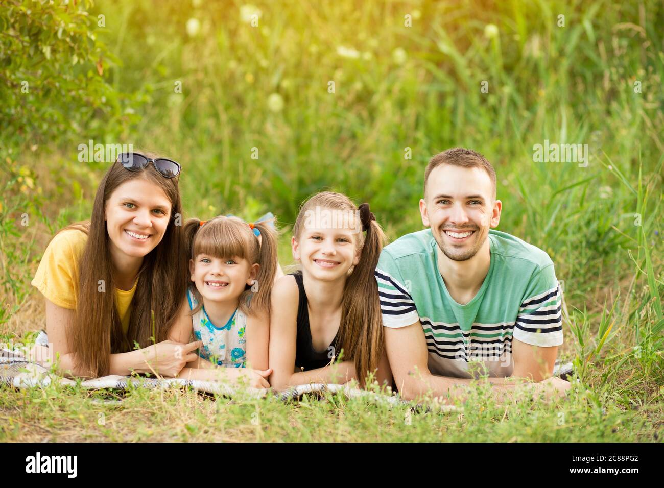 Famille de quatre personnes gaies dans le parc d'été, papa, maman et héritier deux belle fille couchée sur l'herbe et regardant l'appareil photo. Joyeux été avec fa Banque D'Images