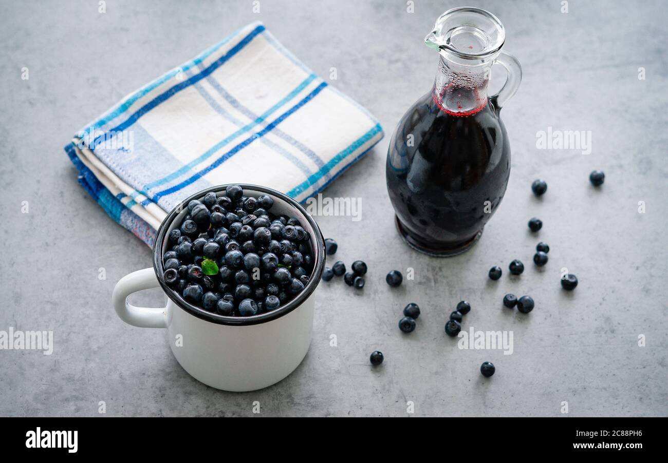 Myrtille fraîche avec des gouttes d'eau dans une tasse blanche. Sirop de myrtille en bouteille ou mélange de verre, sur fond de bois. Banque D'Images