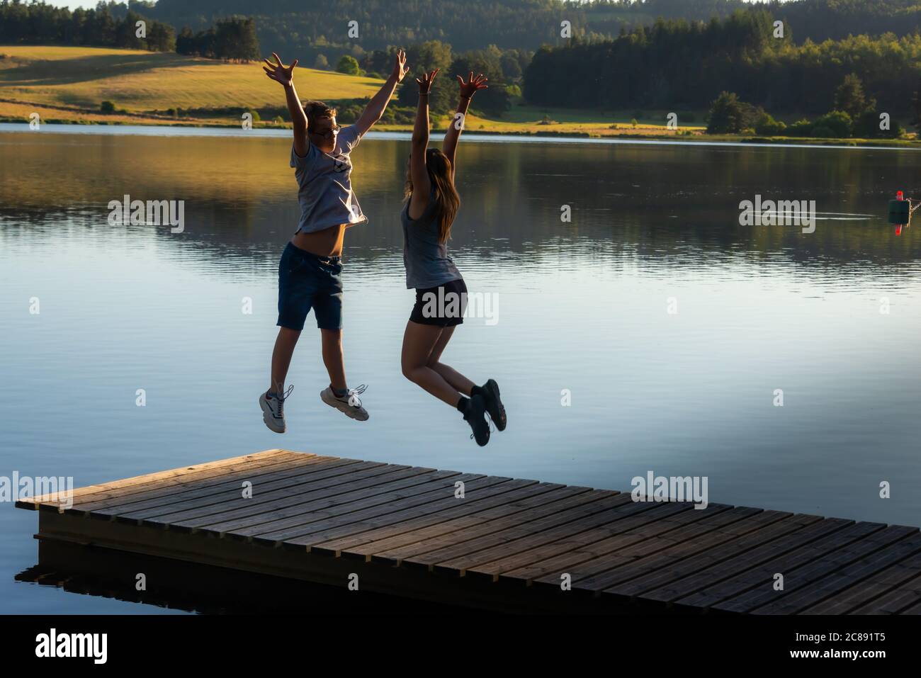Jeune homme et femme sautant les bras dans l'air pour célébrer le succès ou le début des vacances. Debout sur un ponton en bois célébrant le succès Banque D'Images
