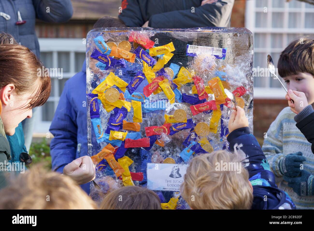 Un groupe d'adultes et d'enfants hack à un morceau de glace avec des cuillères pour atteindre des bonbons et des pièces emballés à The Myths and Legends, York Ice Trail, Angleterre, Royaume-Uni. Banque D'Images