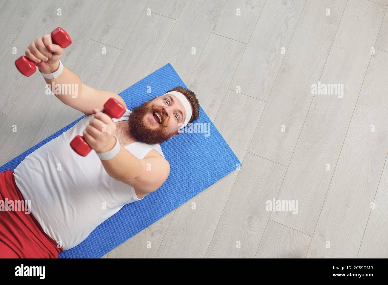 Drôle de gros homme faisant des exercices avec des haltères sur un entraînement sur le sol dans la maison. Banque D'Images