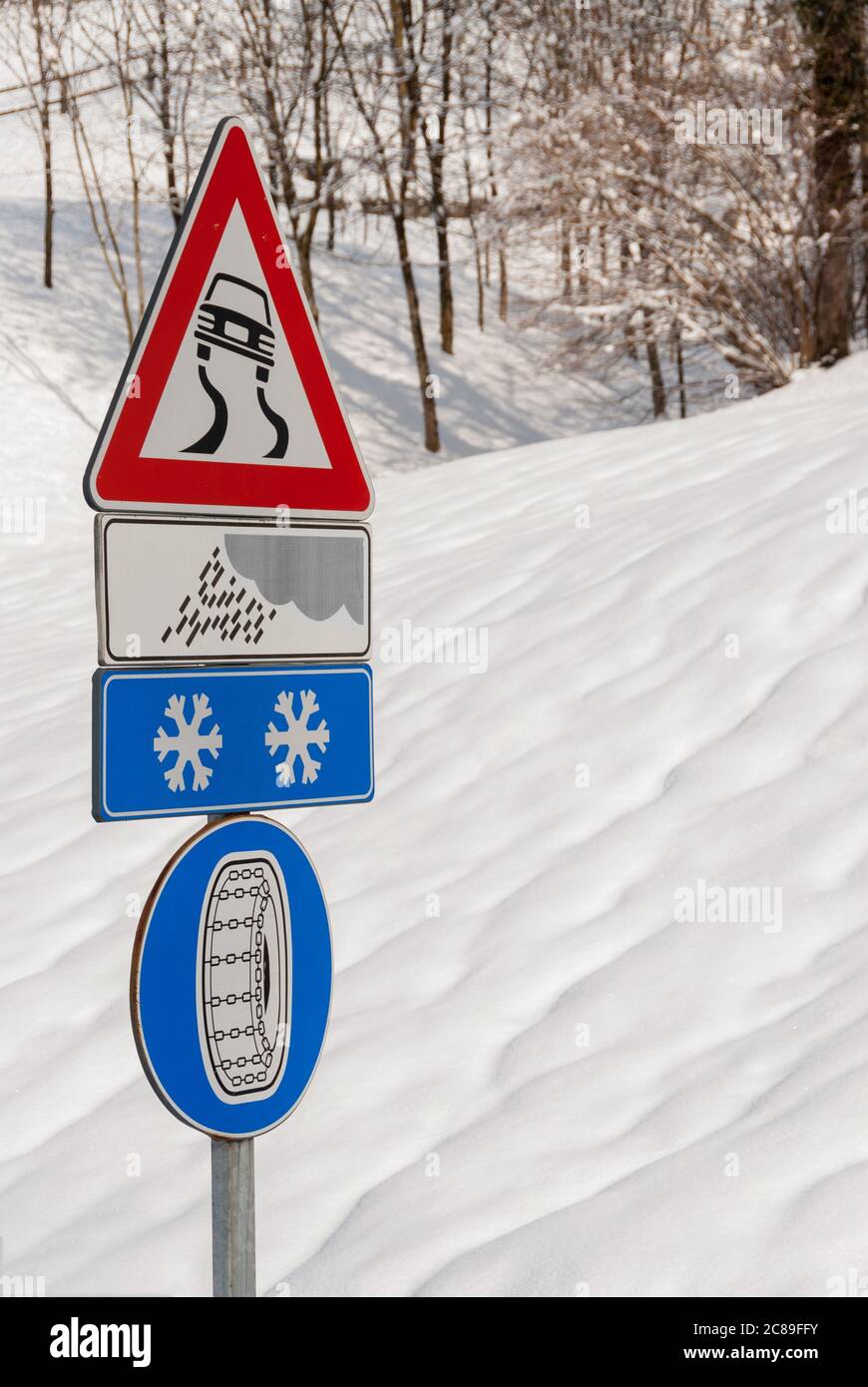 Panneaux d'avertissement pour les routes glissantes dues à la pluie ou à la glace et chaînes à neige obligatoires avec une pente enneigée en arrière-plan Banque D'Images