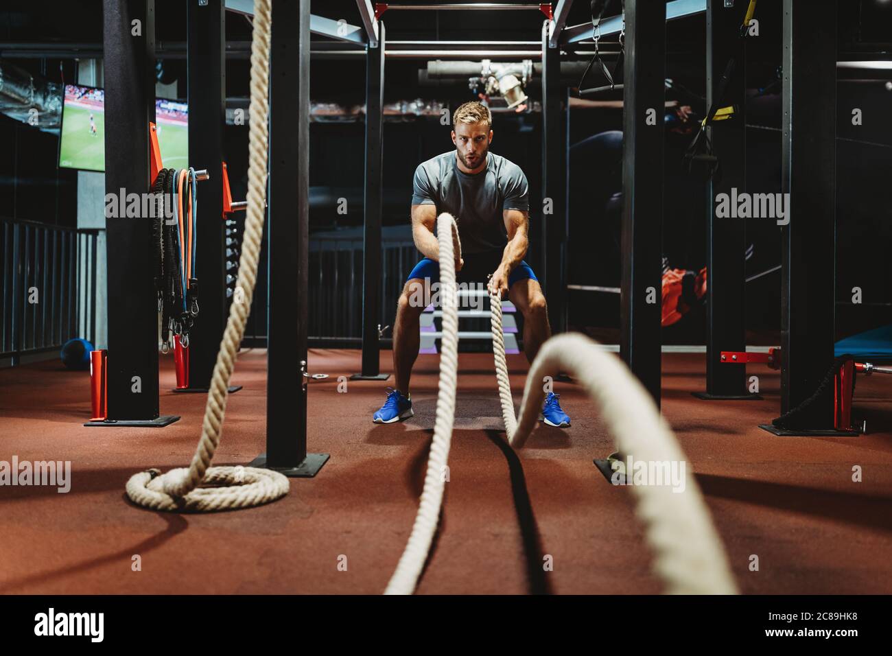 Homme de fitness s'entraîner avec des cordes de combat à la salle de gym. Banque D'Images
