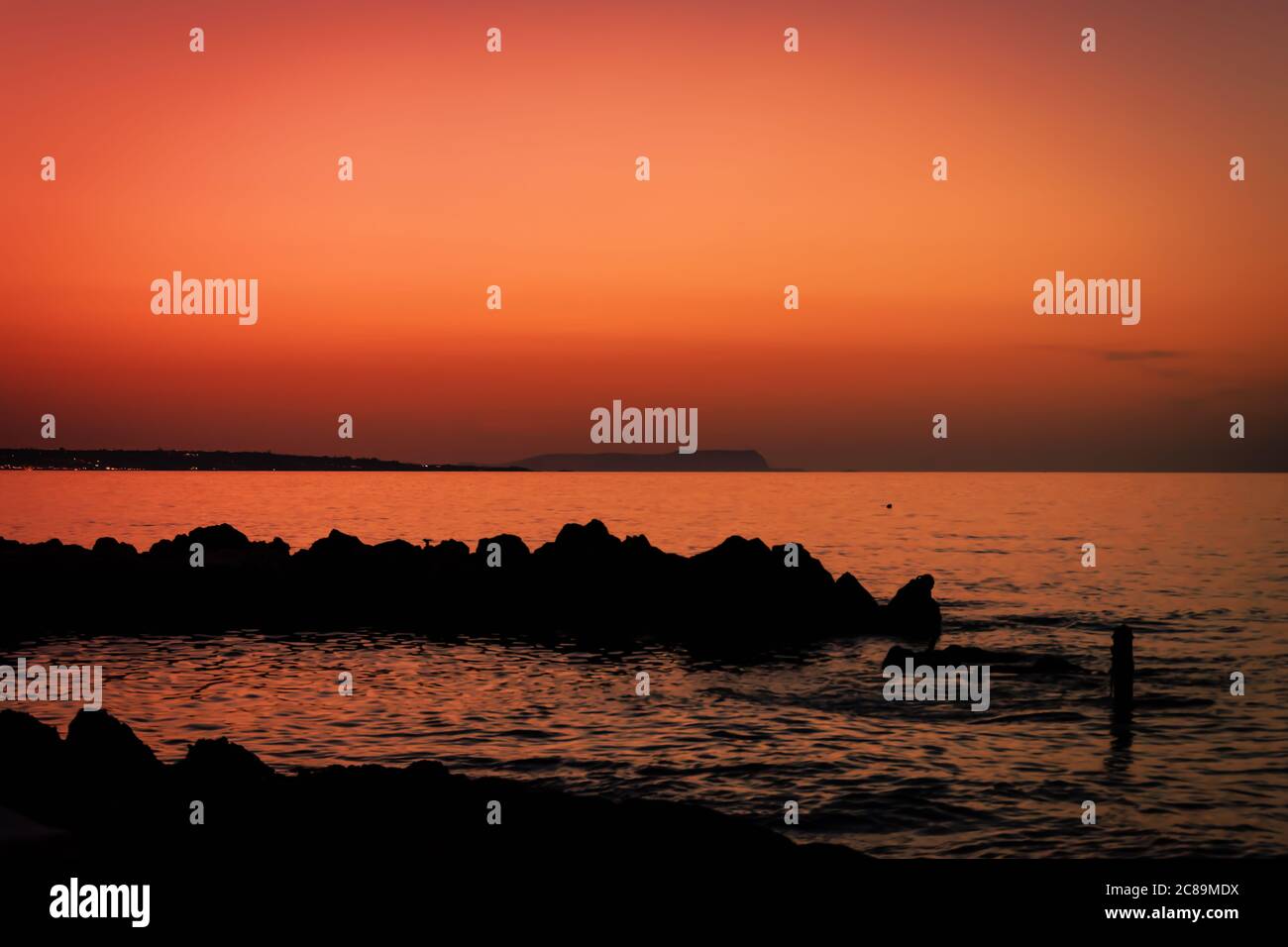 Horizon après le coucher du soleil. Paysage de ciel orange avec silhouette de roche et vagues de l'océan. Coucher de soleil orange sur la rive. Tranquillité au bord de l'eau Banque D'Images