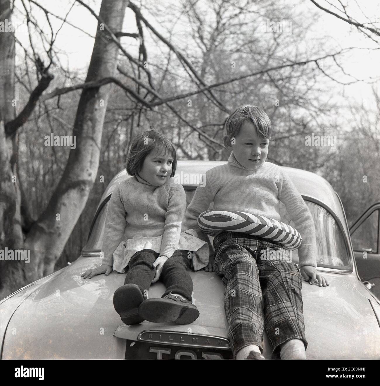 Années 1960, historique, deux jeunes chiildren, un frère et une sœur  portant des pull-overs à col polo assortis, assis sur le botte d'un cocarde  Hillman de l'époque, j'espère que leur père ne