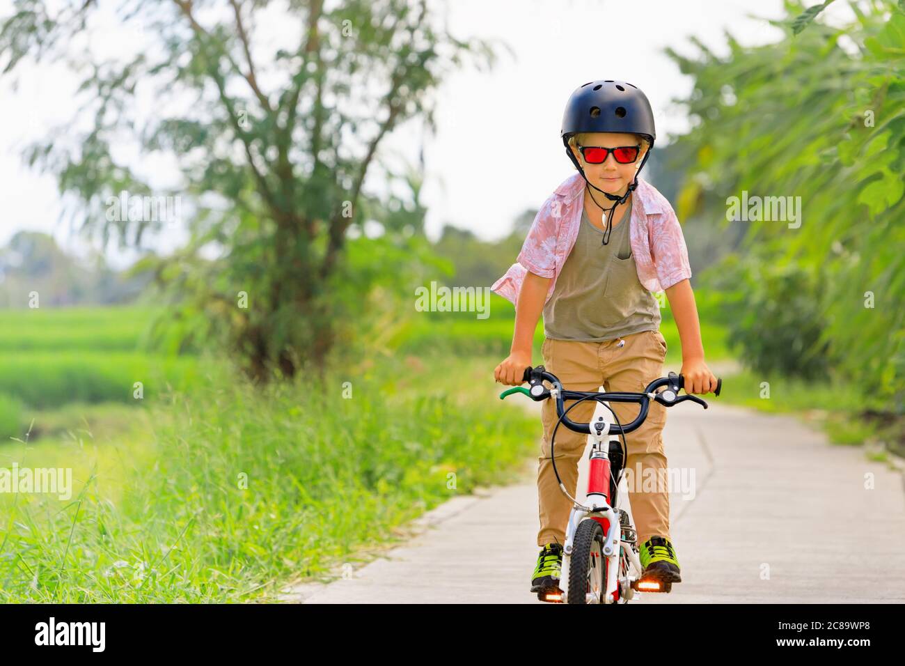 Randonnée à vélo. Jeune rider enfant dans un casque et des lunettes de soleil à vélo. Un enfant heureux s'amuse sur un sentier vide. Vie familiale active, sports Banque D'Images