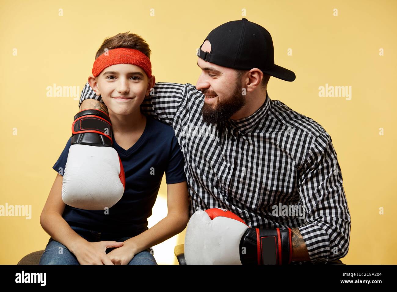 Sport sain Dad barbu et son s'embrassant avec des gants de boxe sur fond jaune Banque D'Images
