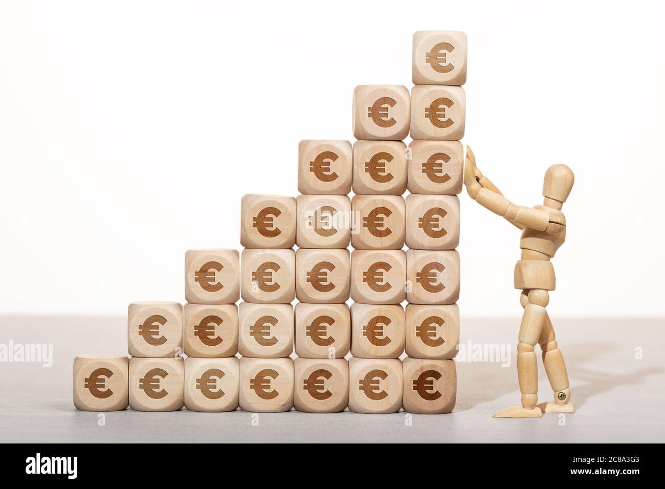 Concept de croissance, de richesse ou de richesse. Mannequin en bois tenant une pile de blocs de bois empilés avec le symbole de l'euro Banque D'Images