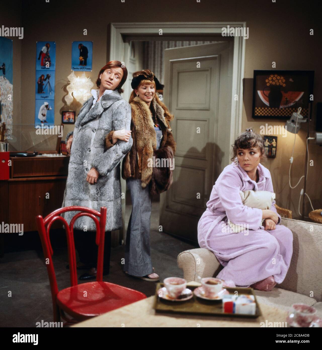 Werner Schulze-Erdel und Ursela Monn als Conni Fuchs gehen gekleidet in Pelz aus, wöhrend Simone Retel als Elfie Pichler im Bademantel auf dem Sofa sitzt in so 'ne und so' ne, Folge 5: Wuschelbär, Regie: Herbert Wise, 1979. Werner Schulze-Erdel et Ursela Monn comme Conni Fuchs vont porter la fourrure tandis que Simone Retel comme Elfi Pichler est assis sur le canapé portant son peignoir dans SO 'ne und so' ne, épisode 5: Wuschelbär, directeur: Herbert Wise, 1979. Banque D'Images