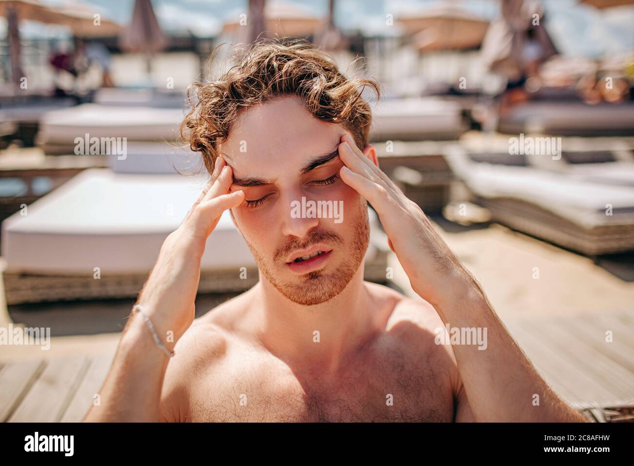 Jeune homme chaud se reposant seul. Un malade avait mal de tête ou de douleur. Symptômes du coronavirus Covid-19. Asseyez-vous seul et souffrez dehors sous le soleil. Maladie Banque D'Images
