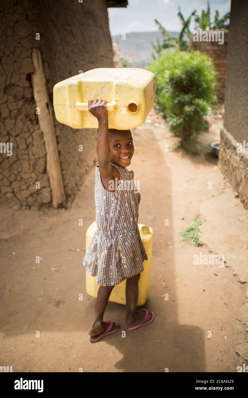 Un jeune enfant heureux récupère de l'eau, transportant des jerricanes sur sa tête, dans le district de Rakai, en Ouganda, en Afrique de l'est. Banque D'Images