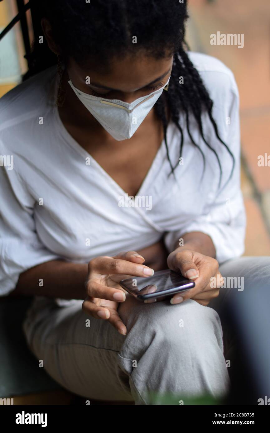 Jeune femme noire dans un masque facial utilisant un smartphone Banque D'Images