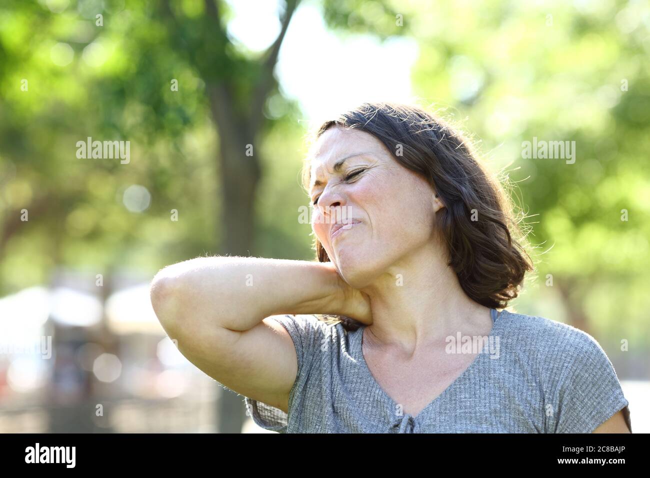 Femme d'âge moyen en douleur souffrant de mal de cou debout dans un parc en été Banque D'Images