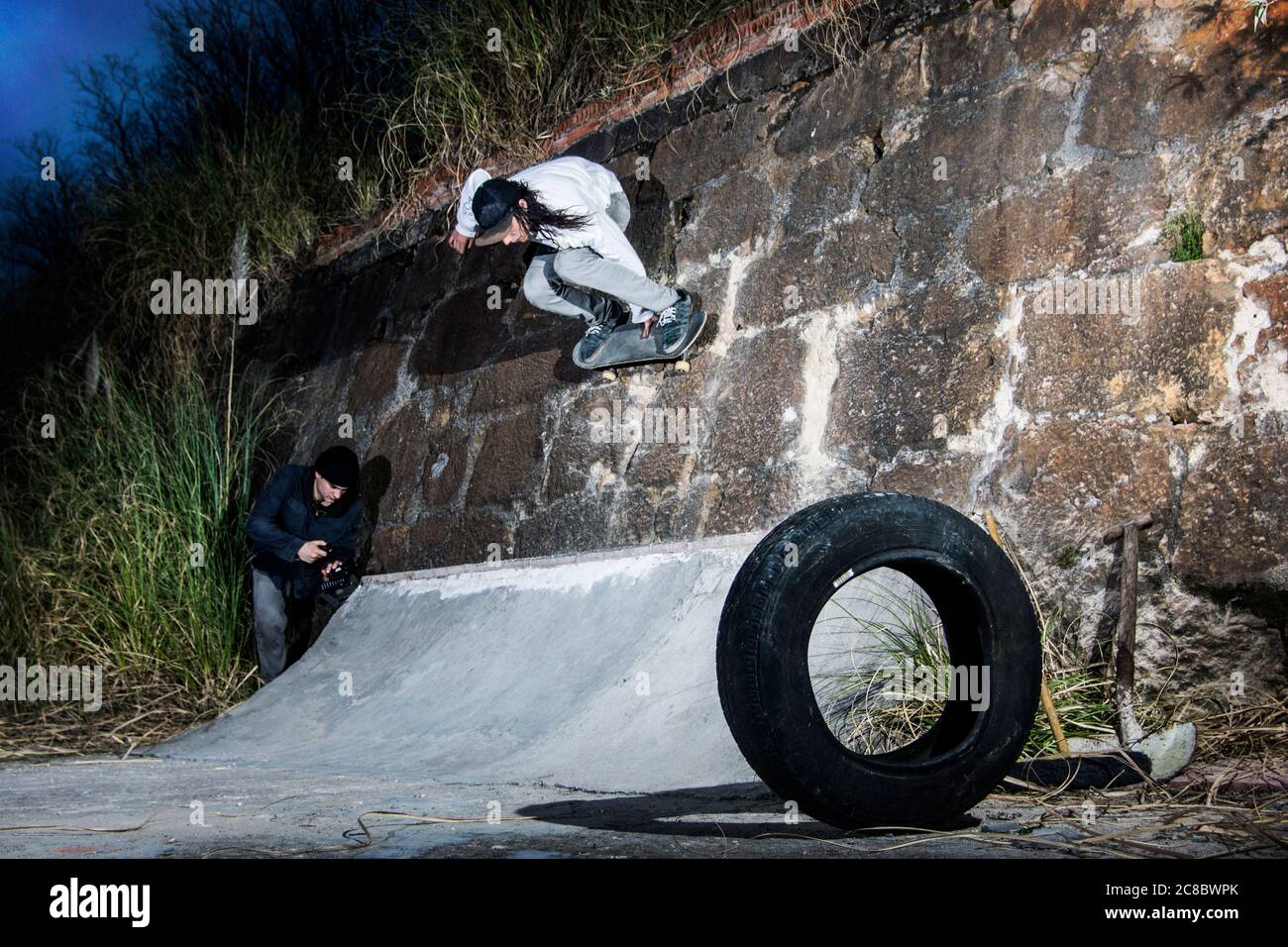 Skateboarder faisant un tour sur un mur de rochers pendant qu'un ami enregistre le moment Banque D'Images