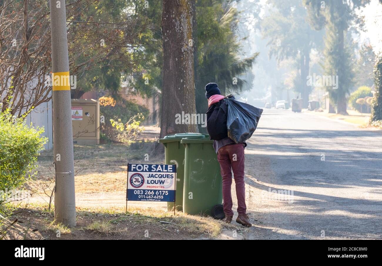 Alberton, Afrique du Sud - un homme noir non identifié se digère dans un bac à foyer à côté d'une propriété à vendre sur une image de chaussée en format horizontal Banque D'Images