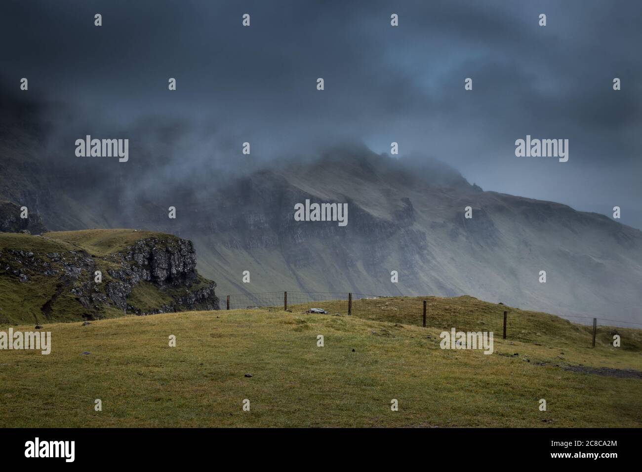 Ein Zaun teult eine hügege, grüne Landschaft mit Bergen und Nebel in Schottland am Old Man of Storr auf der Isle of Skye Banque D'Images