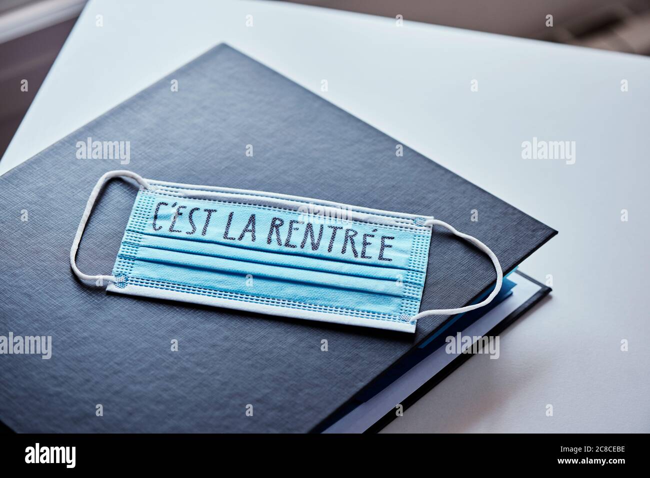 gros plan d'un classeur et d'un masque chirurgical bleu avec le texte de retour à l'école écrit en français, décrivant la nécessité de prévenir l'infection à l'école dans Banque D'Images